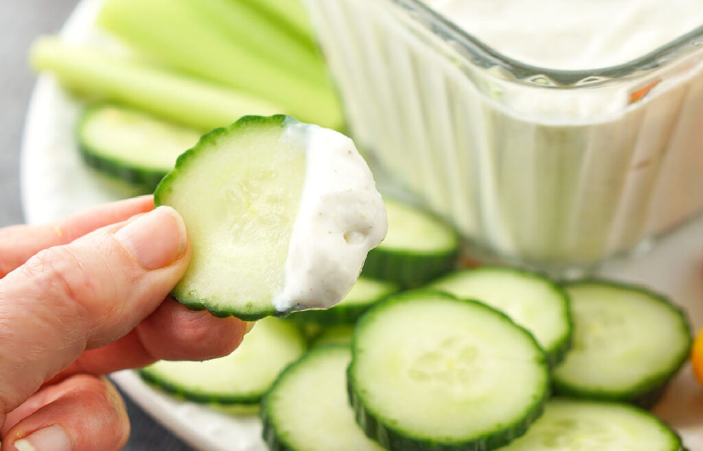 fingers holding a slice of cucumber with dip on it