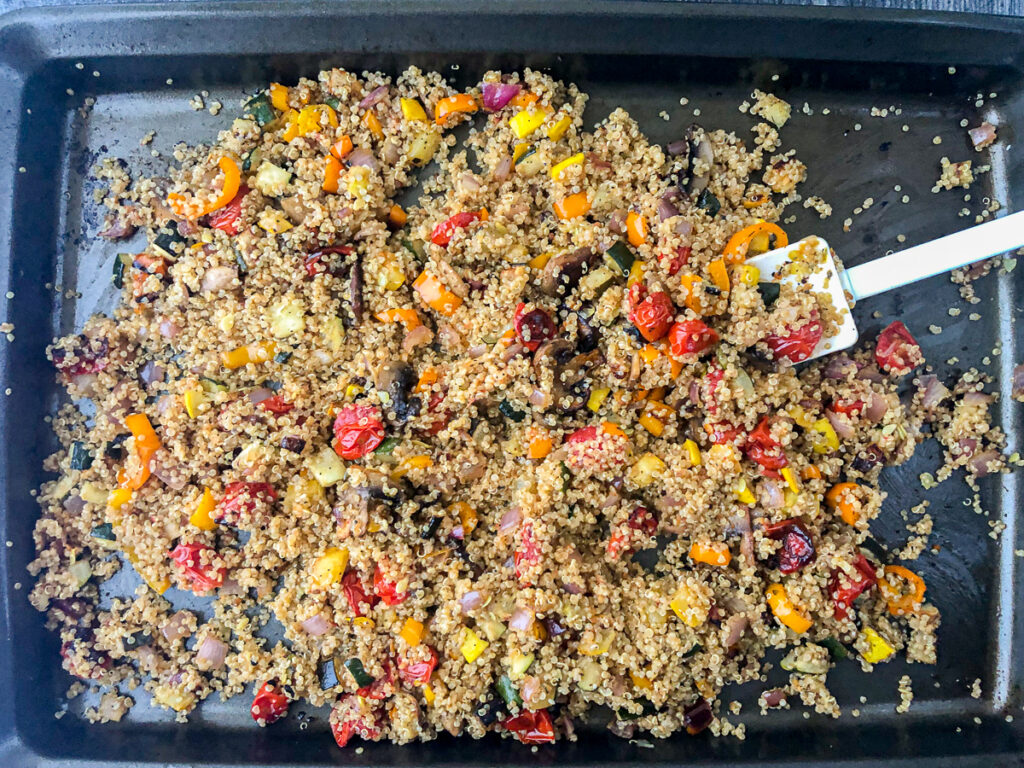 baking sheet with warm quinoa and roasted vegetables mixed up