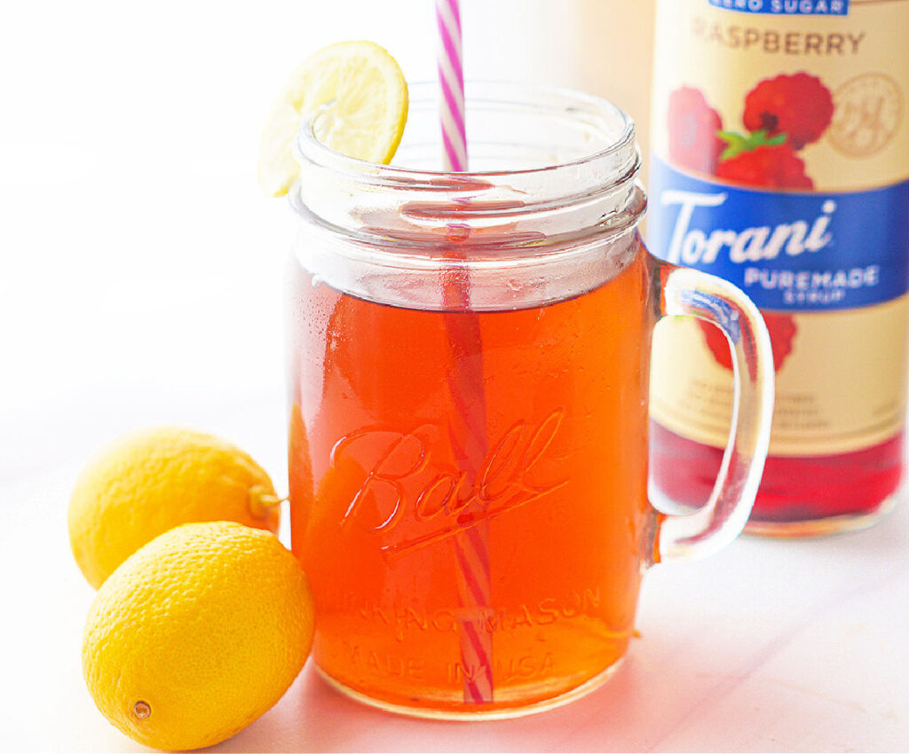 jar glass with keto raspberry tea with fresh lemons and Torani bottle