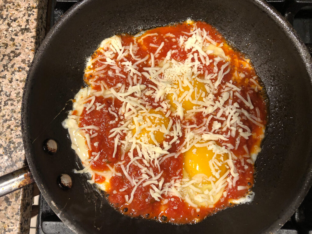 skillet with eggs pizza sauce and cheese cooking