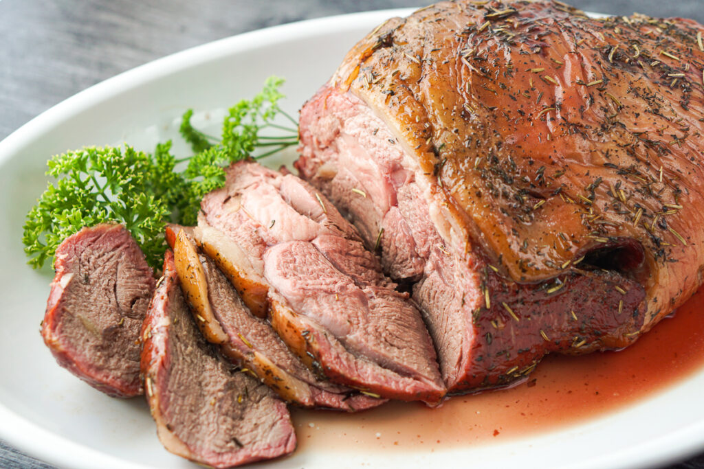 closeup of sliced lamb roast with parsley on a white platter