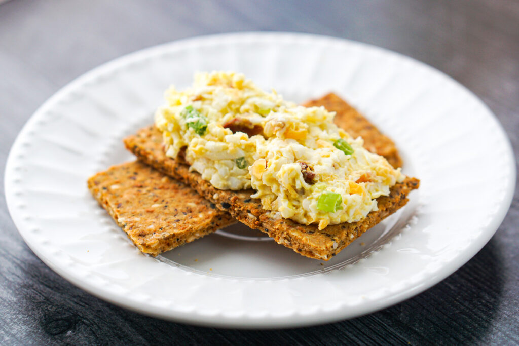 white plate with chopped eggs with bacon on a low carb cracker
