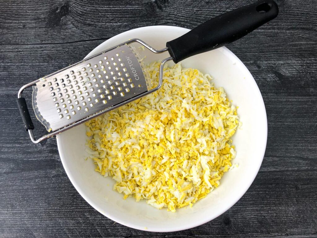 white bowl with grated eggs and a hand grater