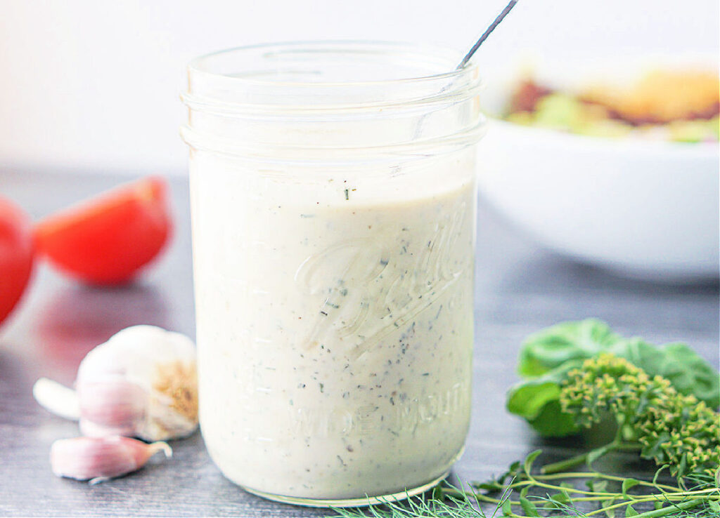 a jar of homemade dairy free ranch dressing and fresh herbs along side