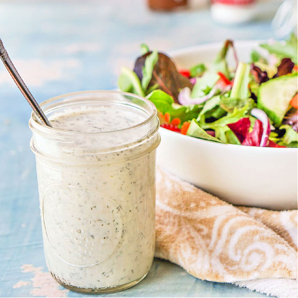 closeup of a jar of homemade dairy free ranch dressing with a salad in th background