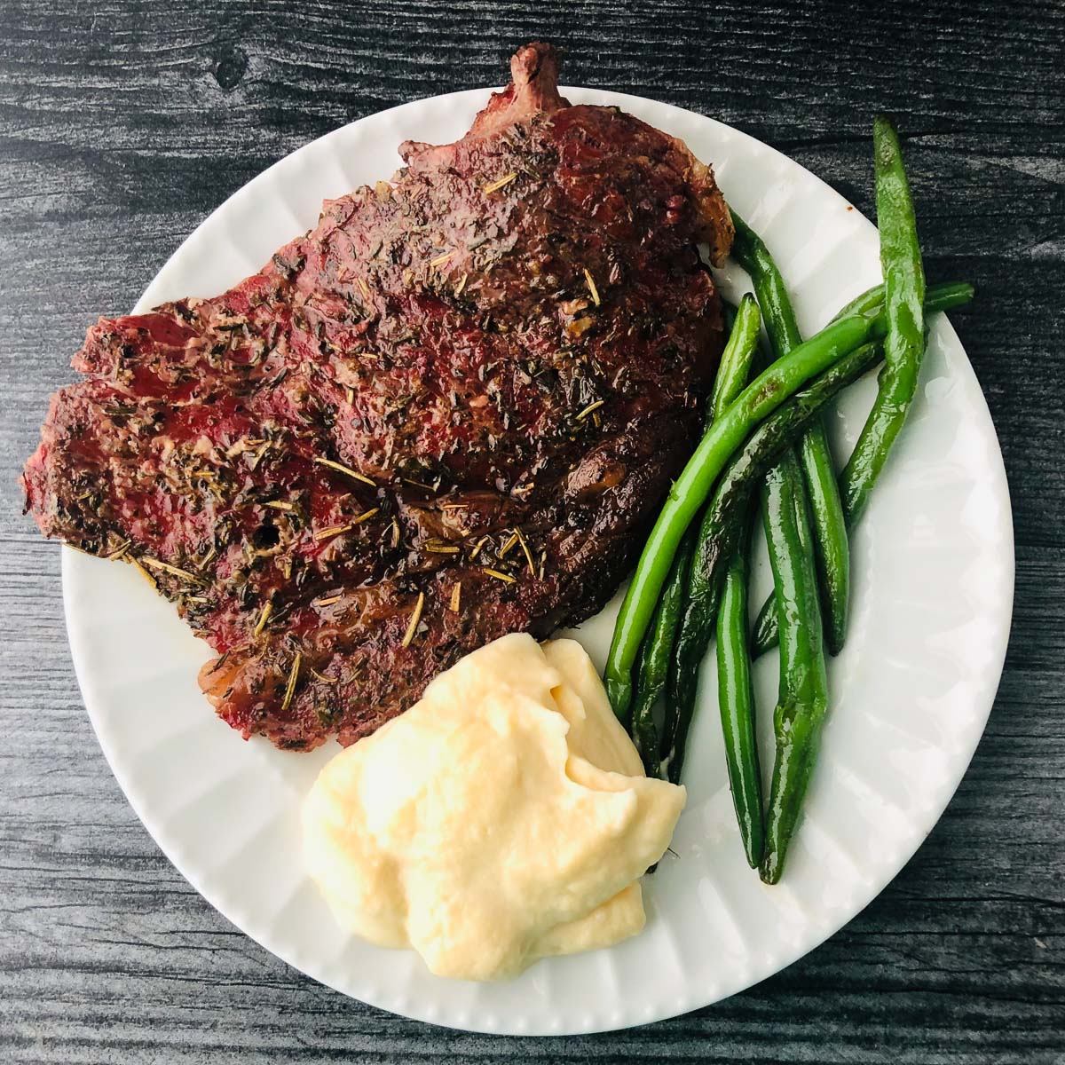 white plate with the end piece of a smoked prime rib with green beans and mashed cauliflower