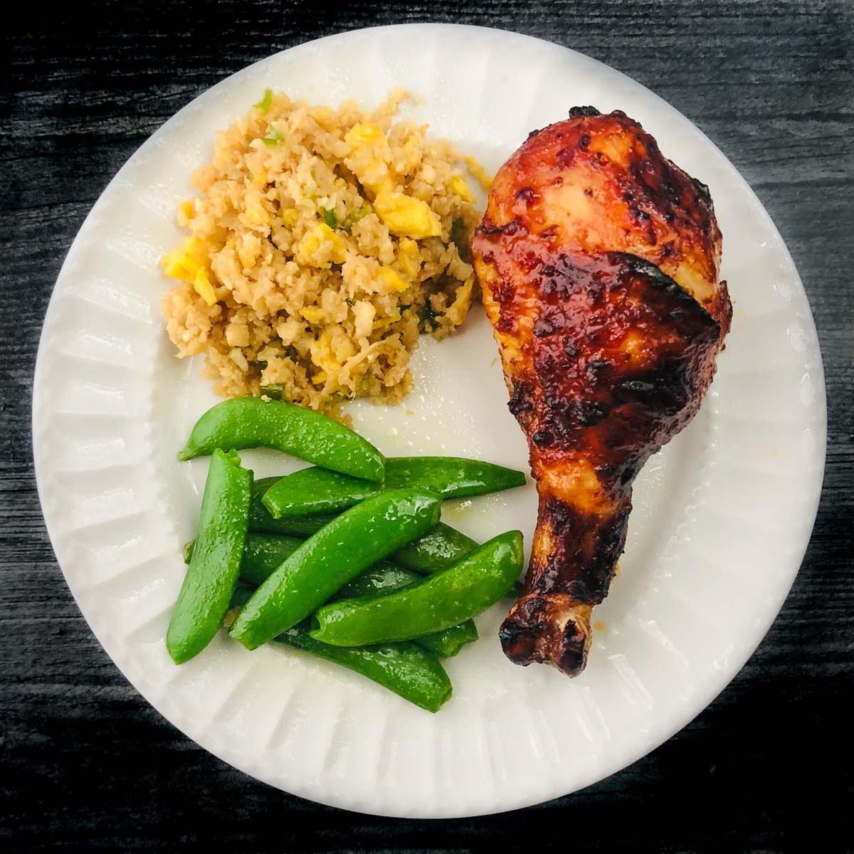 white plate with sticky keto drumsticks, cauliflower rice and snap peas