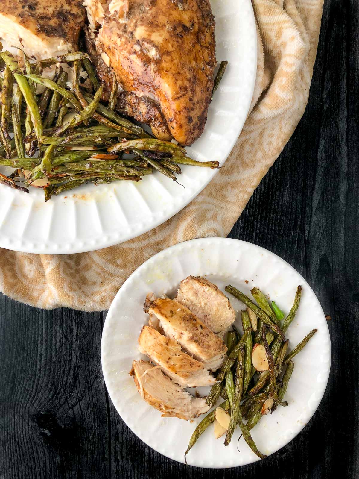 aerial view of white plates with marinated air fryer chicken and green beans with almond slivers