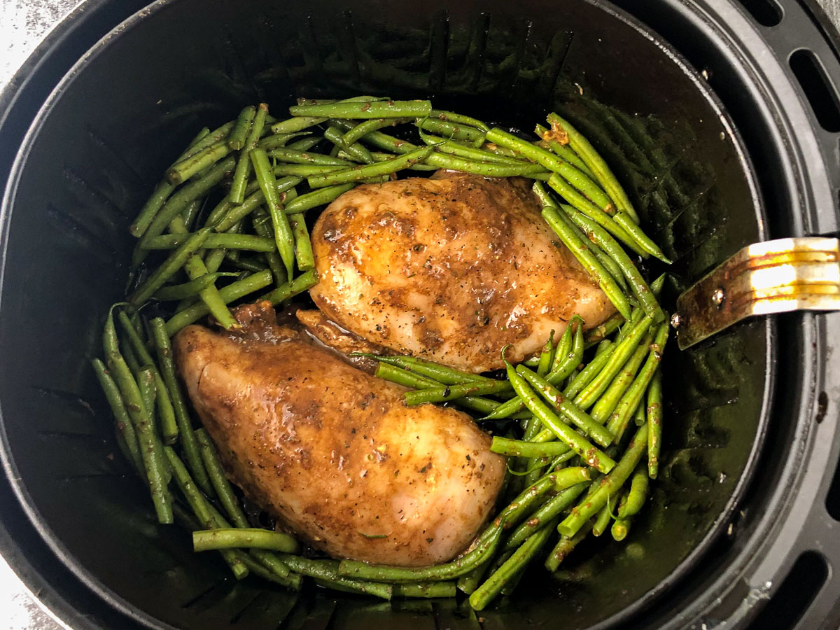 air fryer basket with raw chicken and green beans in a balsamic sauce