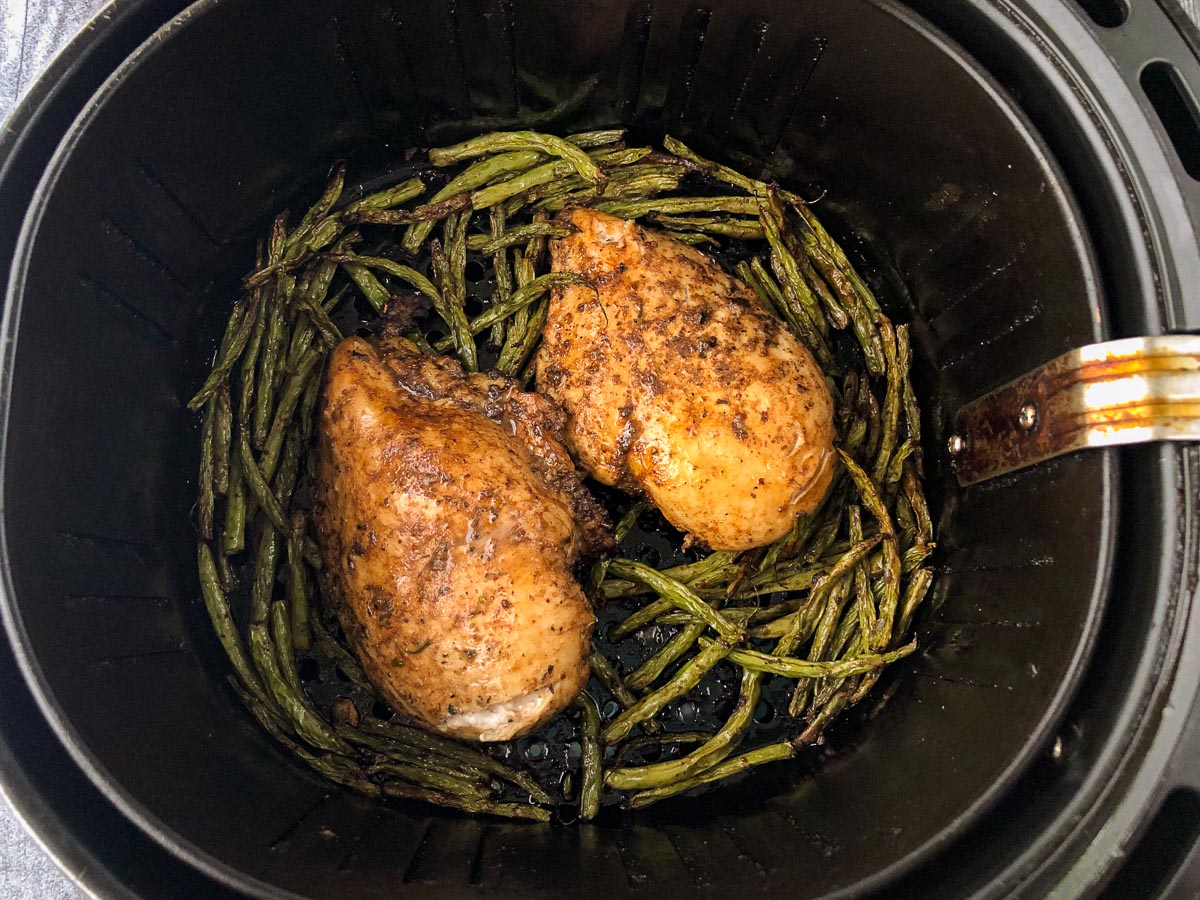 air fryer basket with finished roasted chicken and beans