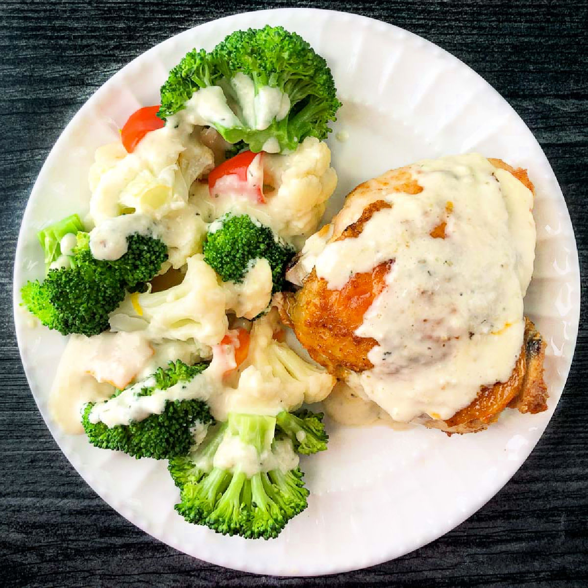 white plate with crispy chicken thighs and veggies with creamy parmesan garlic sauce