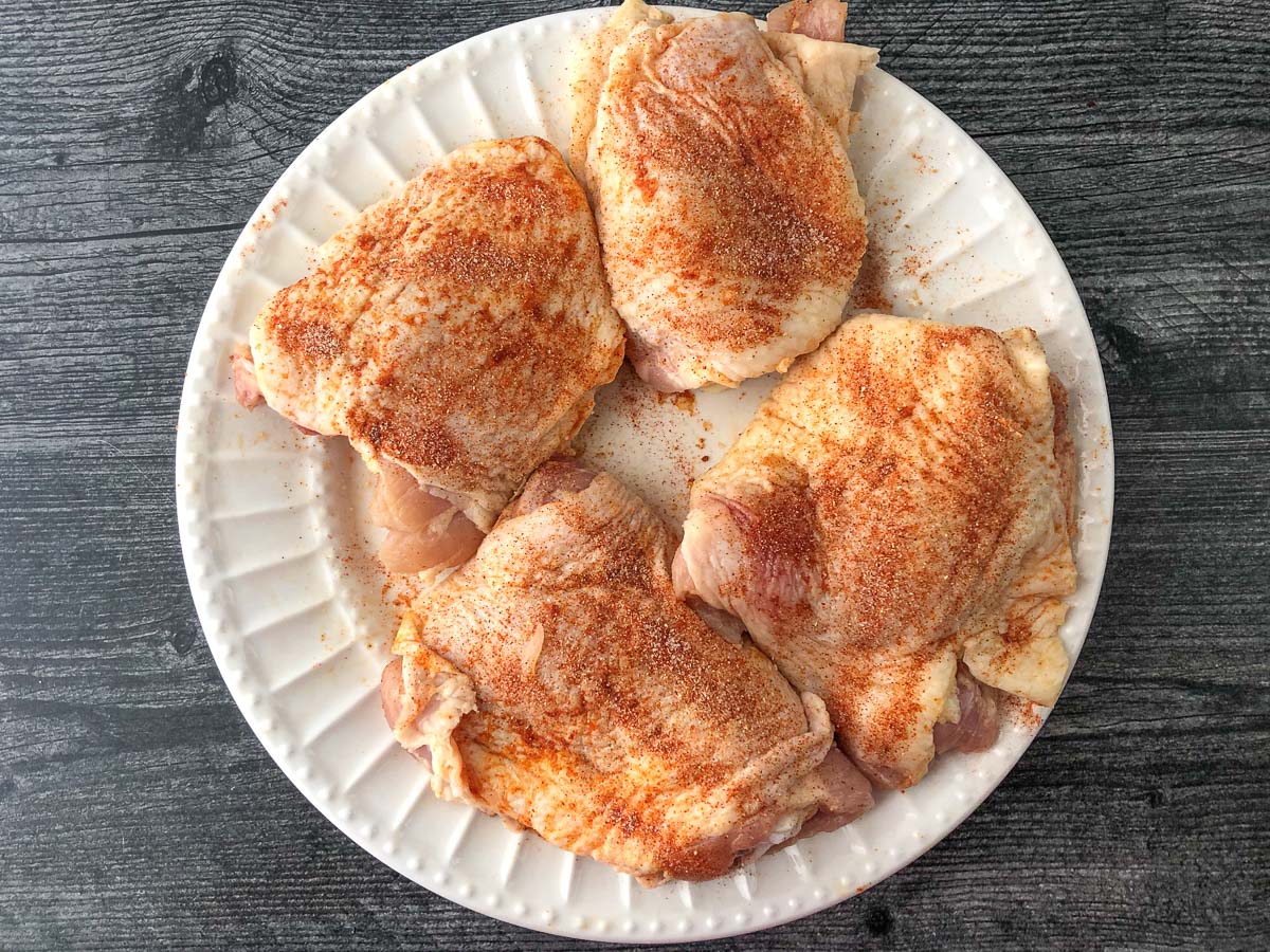 raw chicken thighs on a plate with seasonings on them