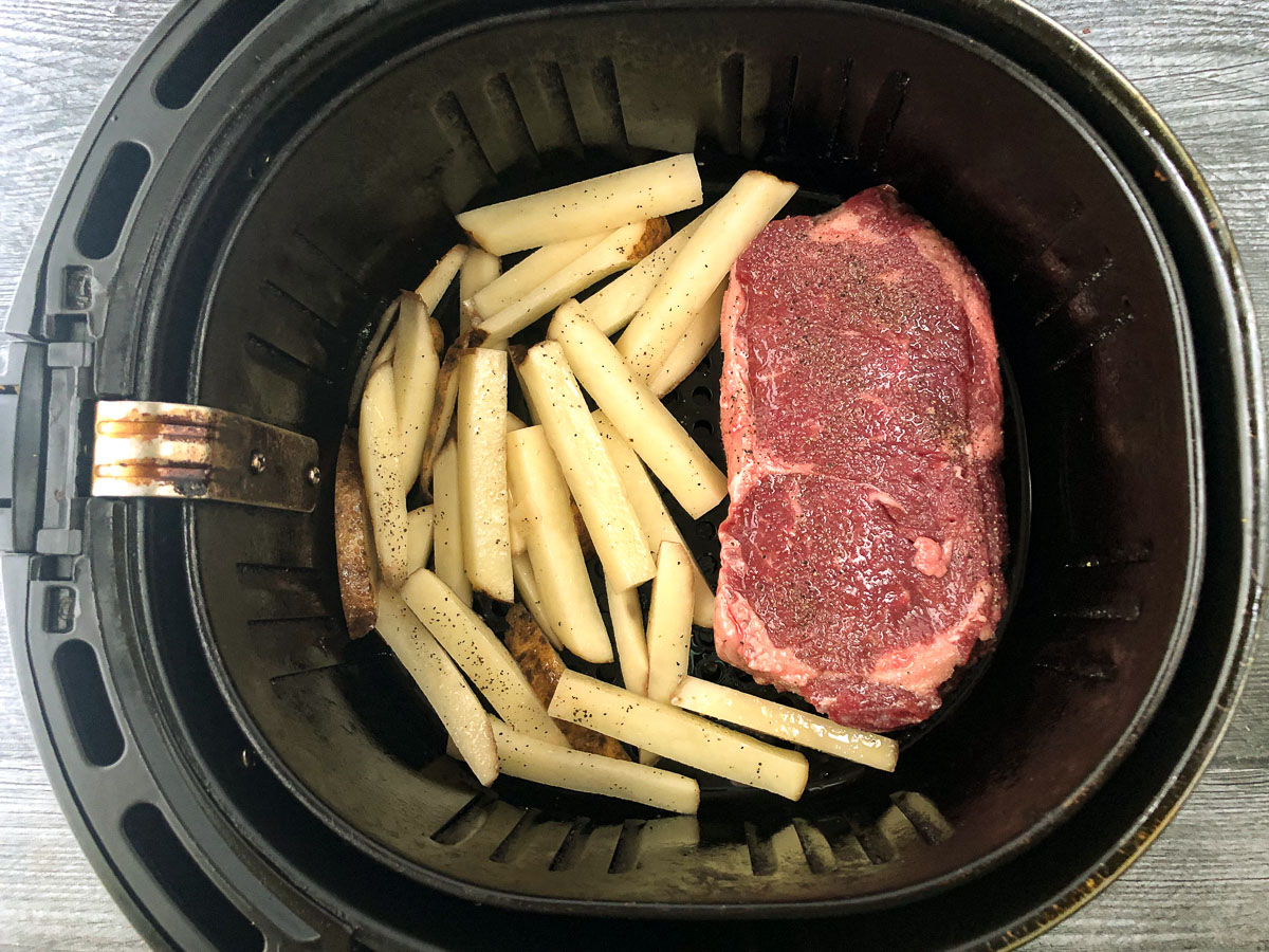 air fryer basket with raw steak and raw fries