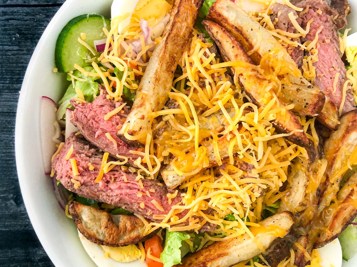Ariel view of a white bowl with fries and steak salad topped with cheese