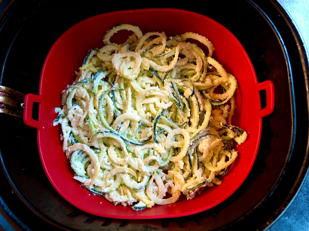 air fryer basket with red liner and raw zucchini noodles with cheese