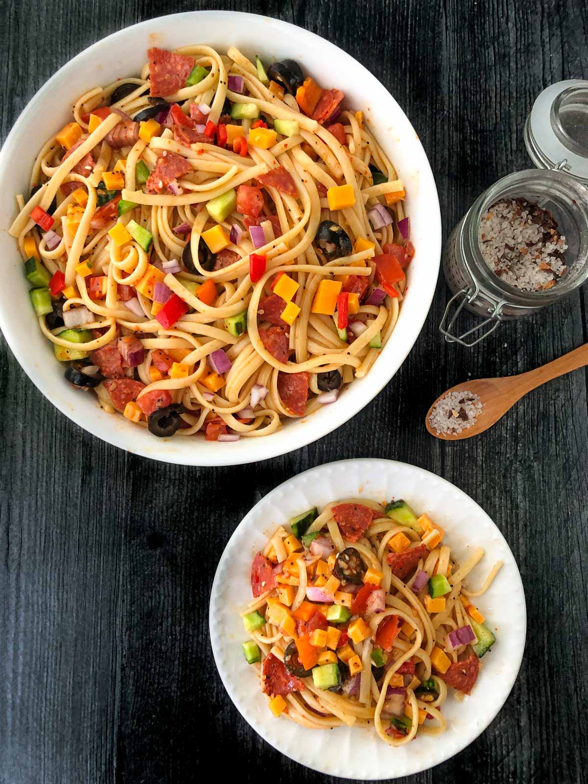 aerial view of white bowl and plate with cold pasta salad with cheese and pepperoni