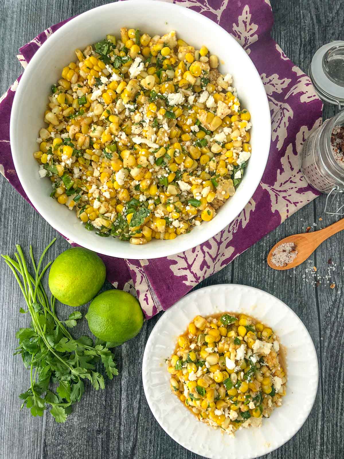 aerial view of white bowl and plate with corn salad and fresh limes and cilantro