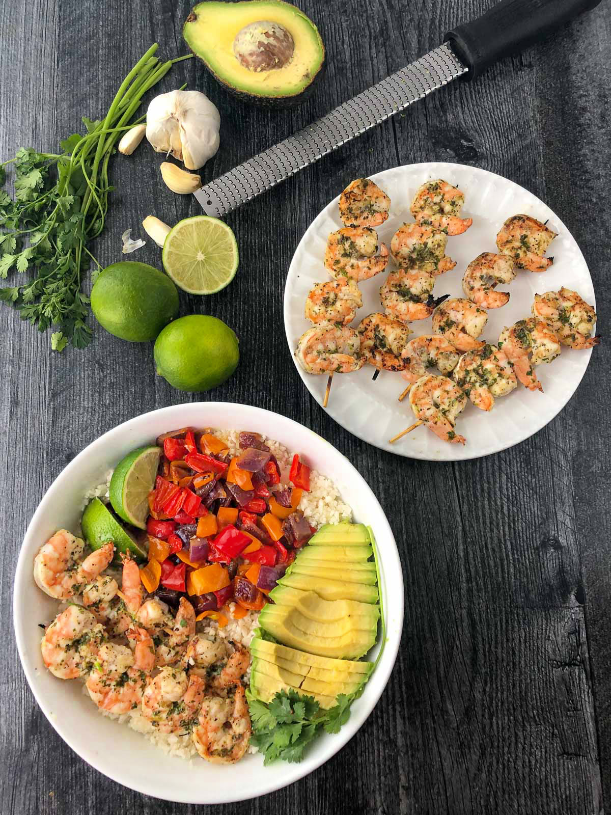 aerial view of a plate grilled keto shrimp kebabs and a shrimp rice bowl with fresh limes, avocado and cilantro