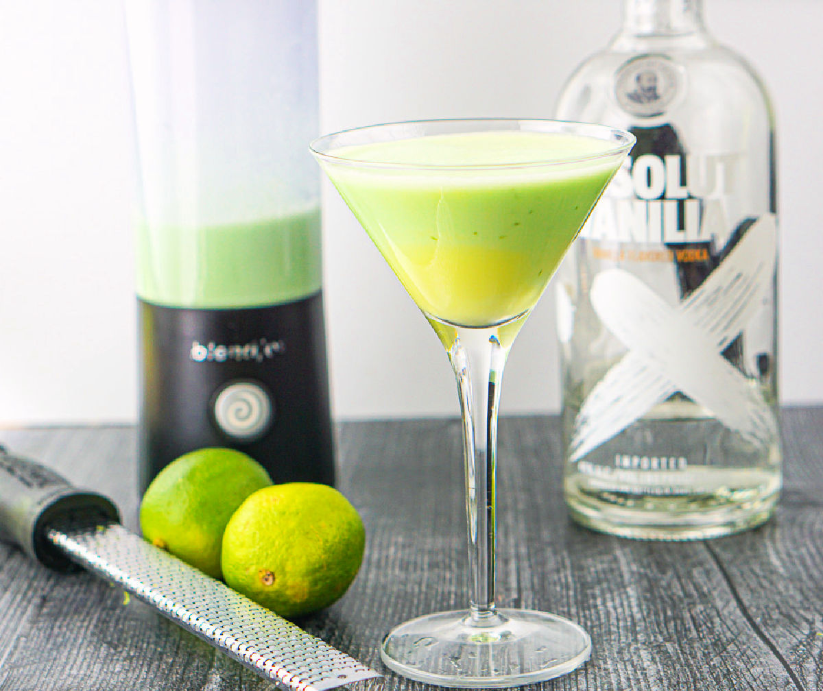 martini glass with a key lime cocktail and a mini USB blender, microplane and limes