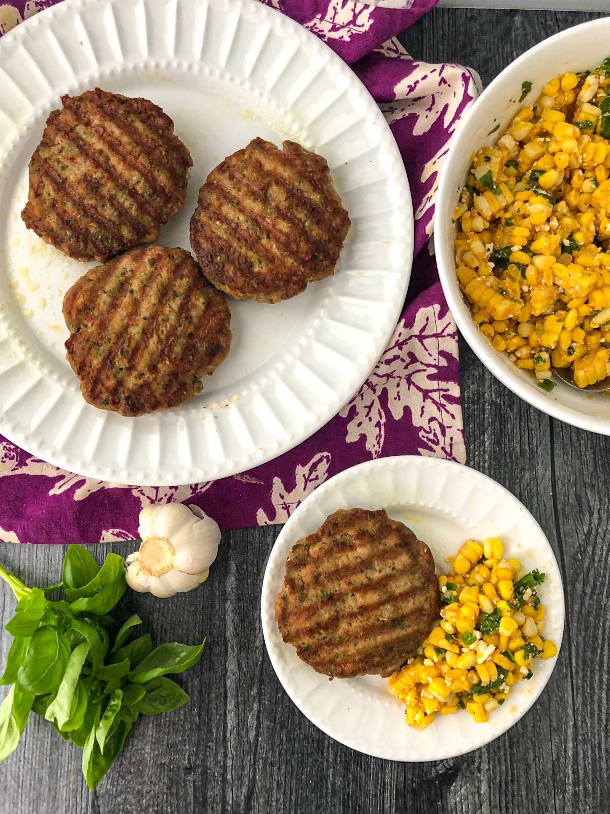 aerial view of white plates with burgers and a bowl of Mexican corn salad