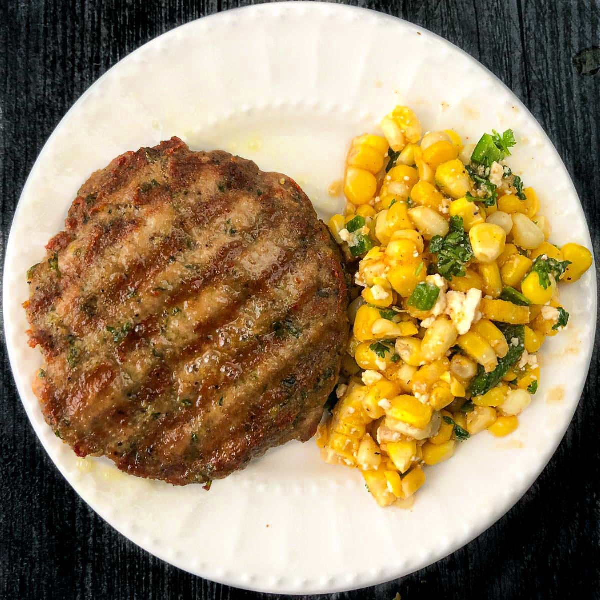 white plate with keto pesto turkey burger and some street corn salad