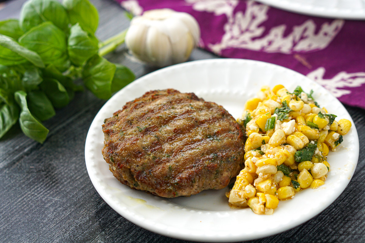 white plate with turkey burger and corn and fresh basil sprigs with garlic cloves