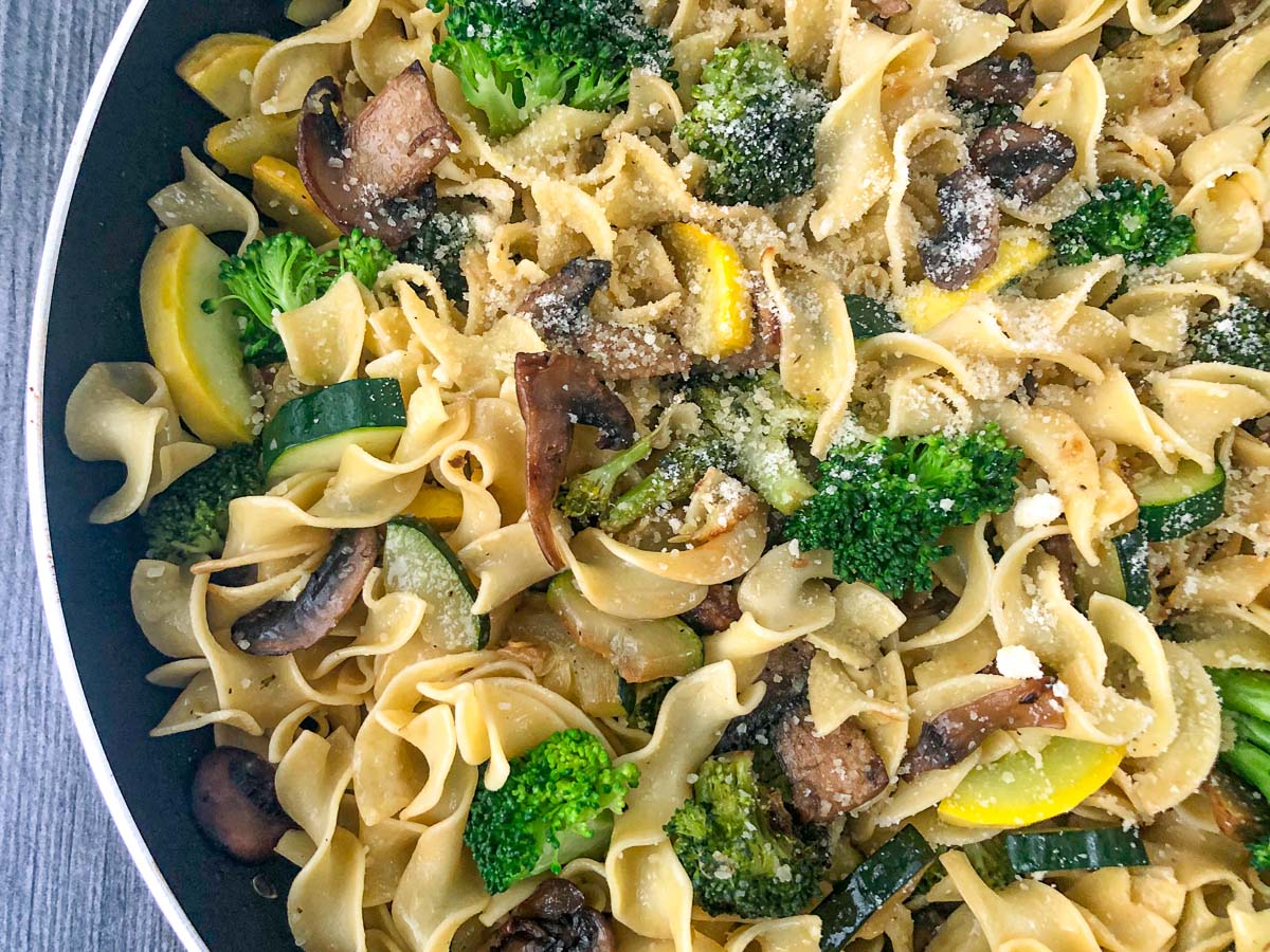 closeup of a skillet with egg noodles and sautéed garlic veggies