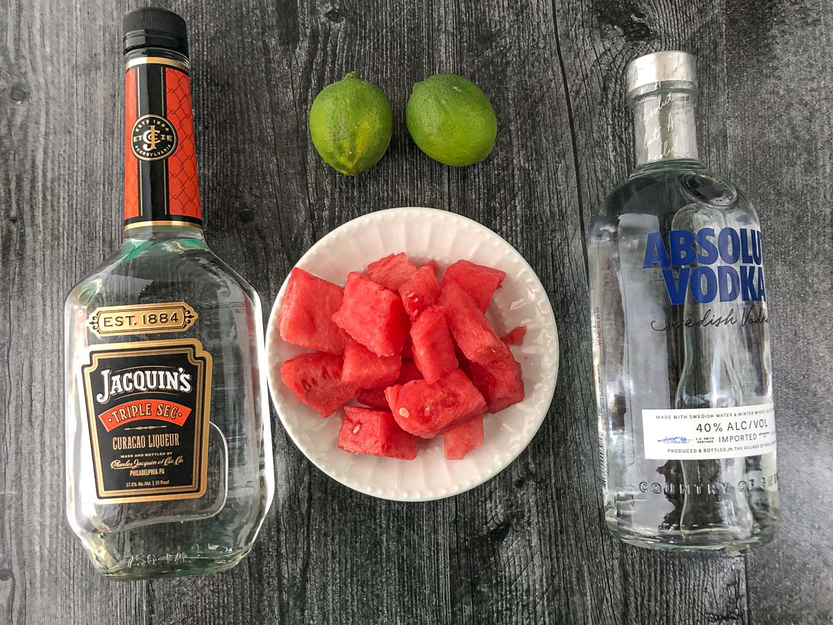 triple sec bottle and vodka bottle with chunks of watermelon and limes