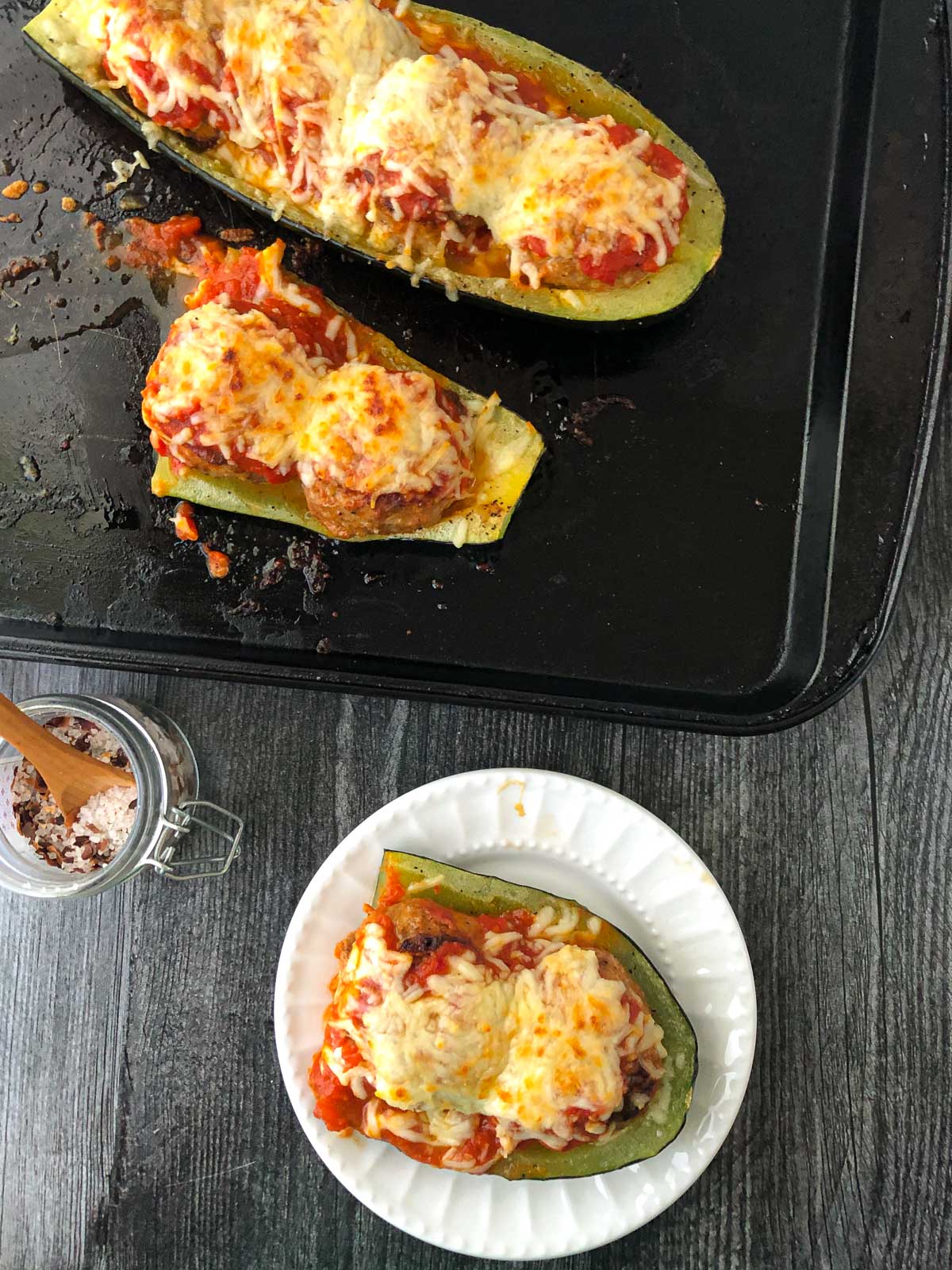 aerial view of a baking sheet with keto zucchini boats and white plate with a piece of one