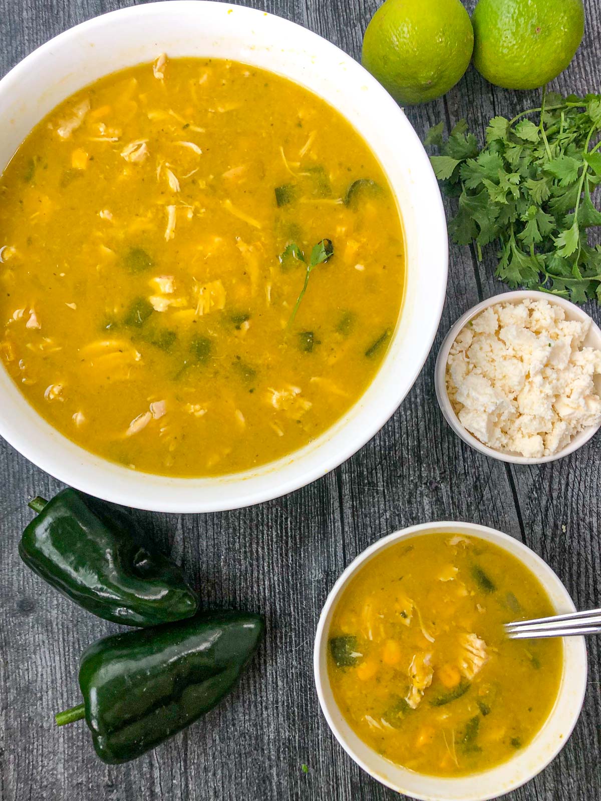 aerial view of two white bowls with corn chowder with a bowl of queso cheese and fresh poblano and fresh cilantro