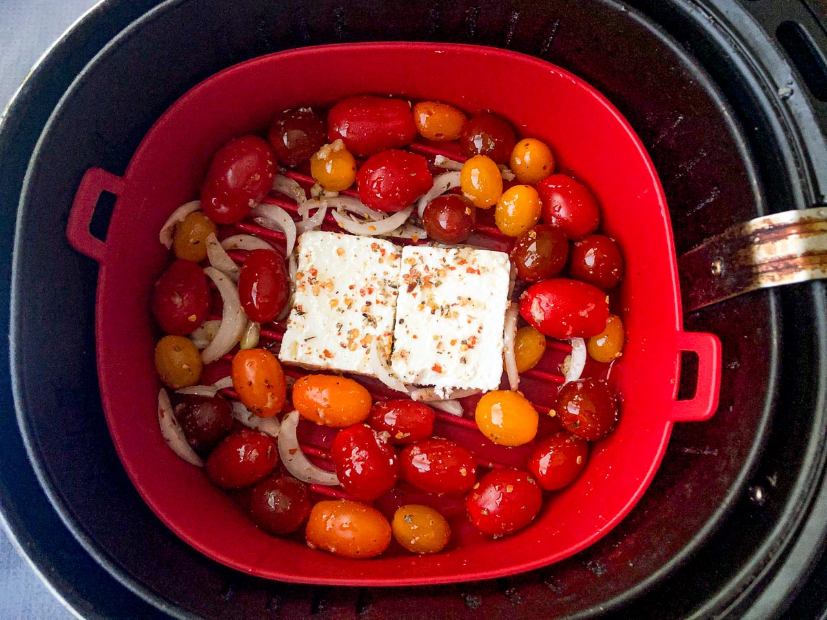 air fryer basket with raw tomatoes and a block of feta
