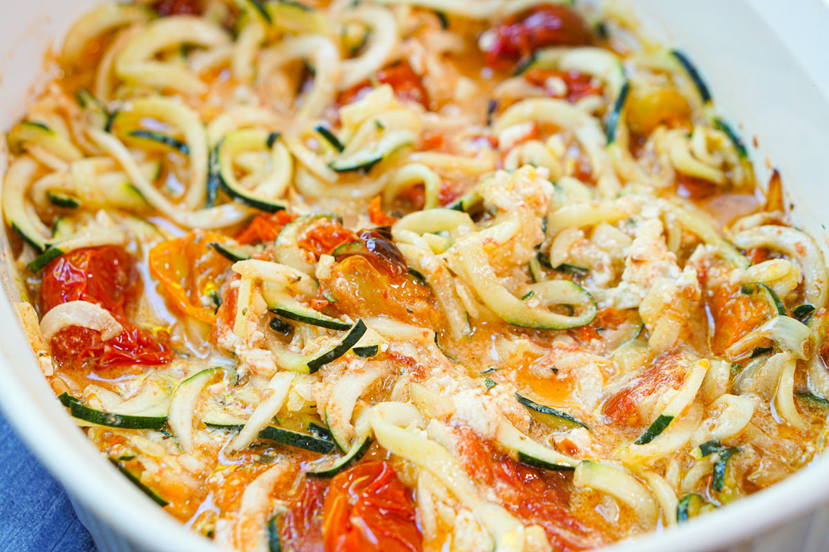 closeup of a baking dish with zucchini pasta and baked feta with tomatoes