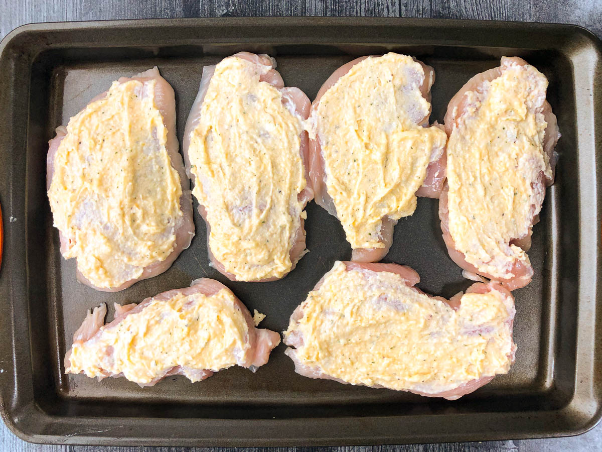 baking sheet with raw pieces of chicken covered in cheese mixture