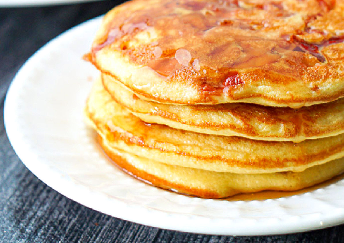 closeup of a stack of bacon pancakes with sugar free syrup on white plate