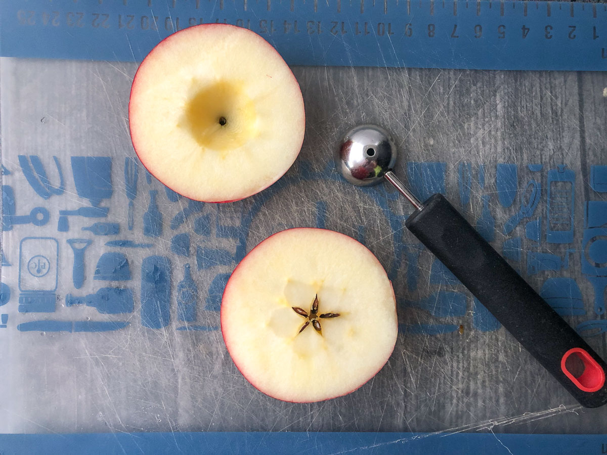 cutting board with an apple cut in half and a melon ball scoop