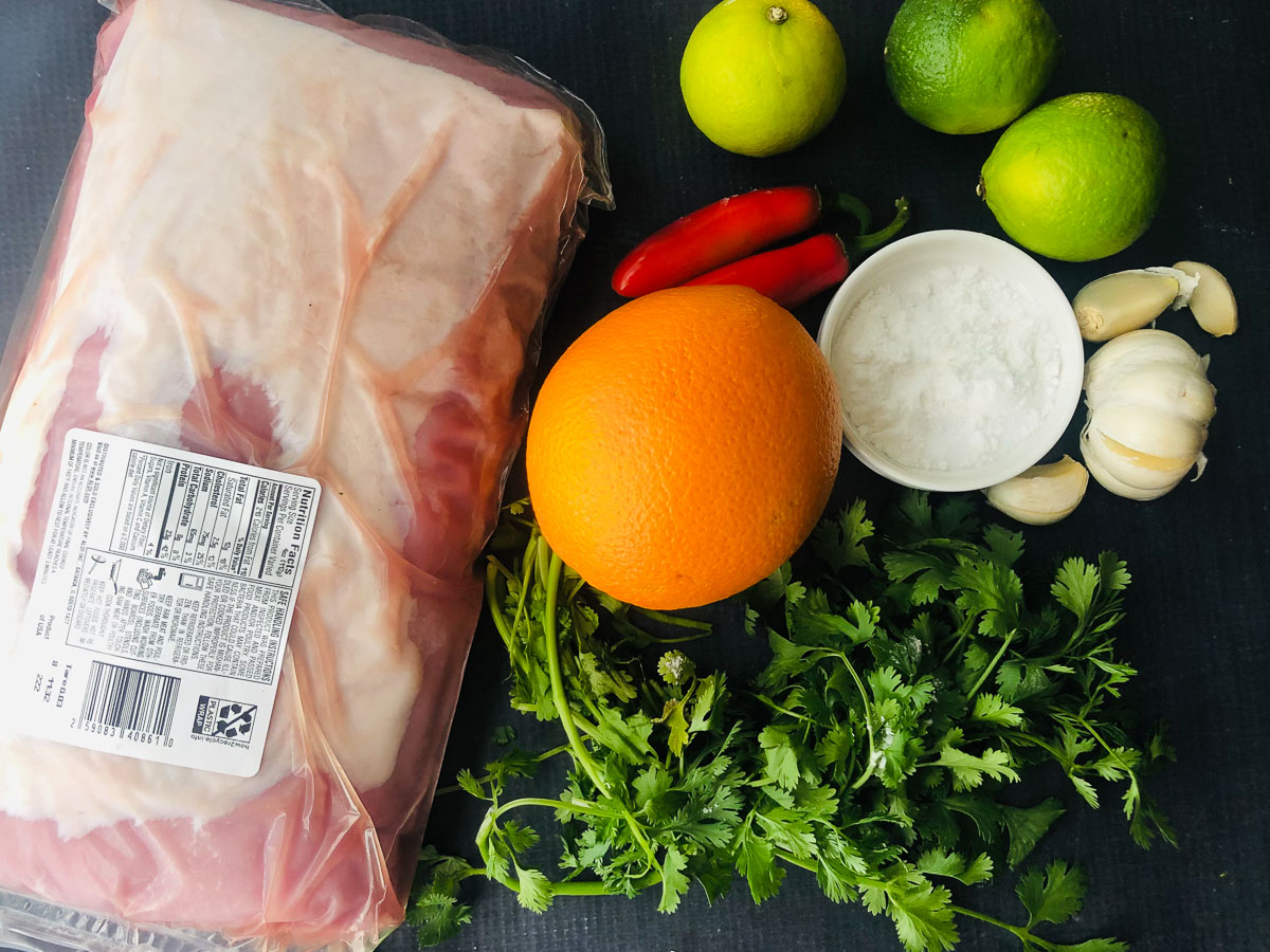 recipe ingredients - pork loin roast, limes, oranges, sugar, garlic and peppers and cilantro
