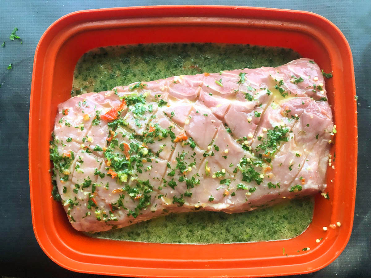 marinating container with raw pork loin marinated in mojo sauce
