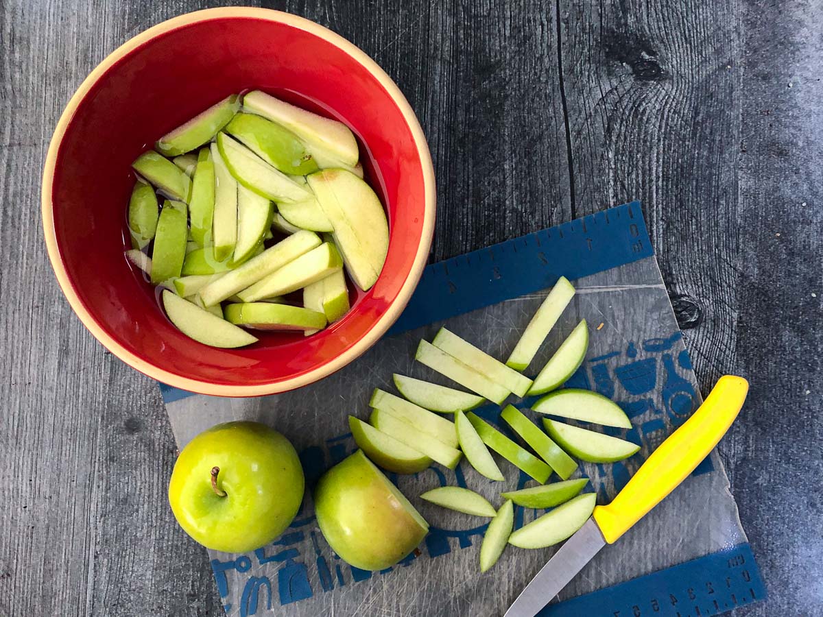 cutting board with slices of green apples and red bowl
