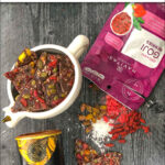 aerial view of healthy chocolate bark in a white bowl and cocoa powder and goji berry bag with text