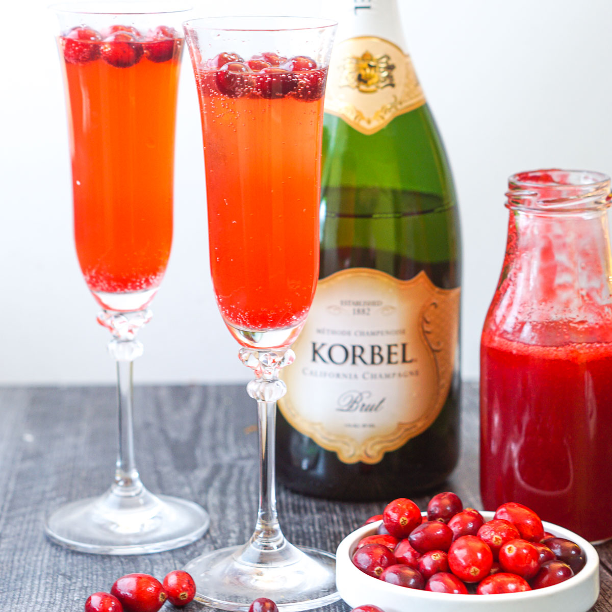 2 champagne glasses with keto cranberry mimosa and a champagne bottle and fresh cranberries