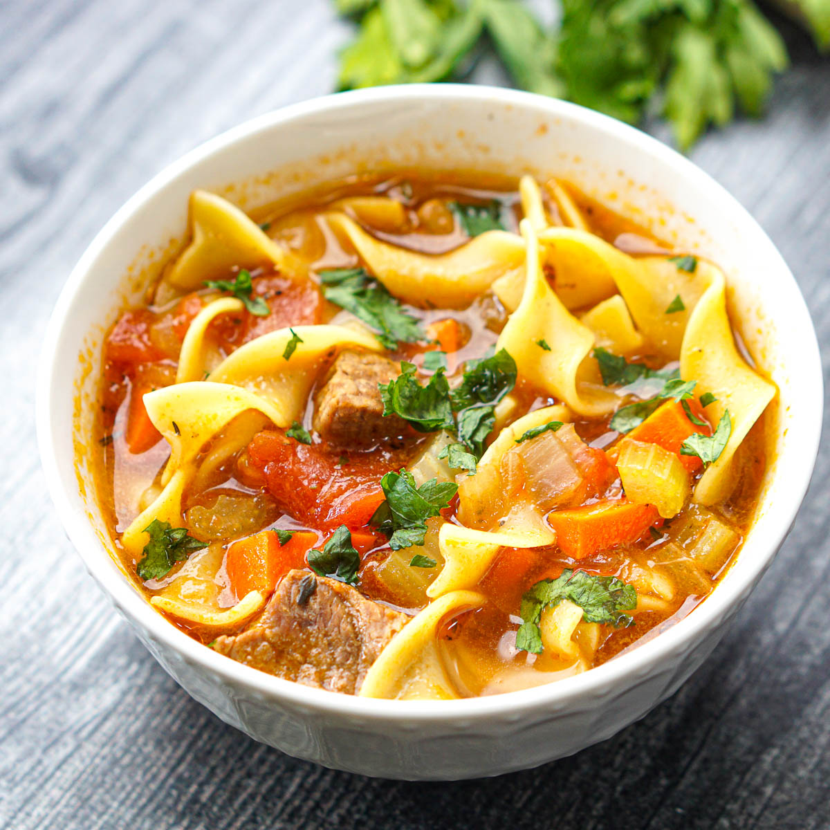 white bowl with vegetable beef noodle soup with fresh parsley