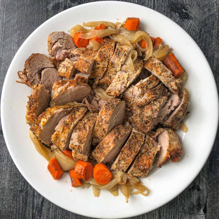 white platter with sliced pork tenderloin and roasted veggies made in slow cooker