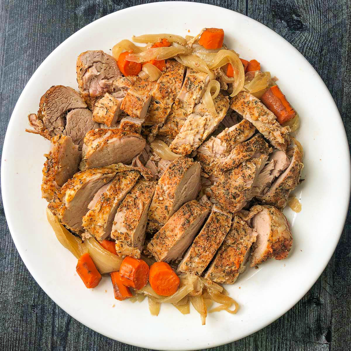 white platter with sliced pork tenderloin and roasted veggies made in slow cooker