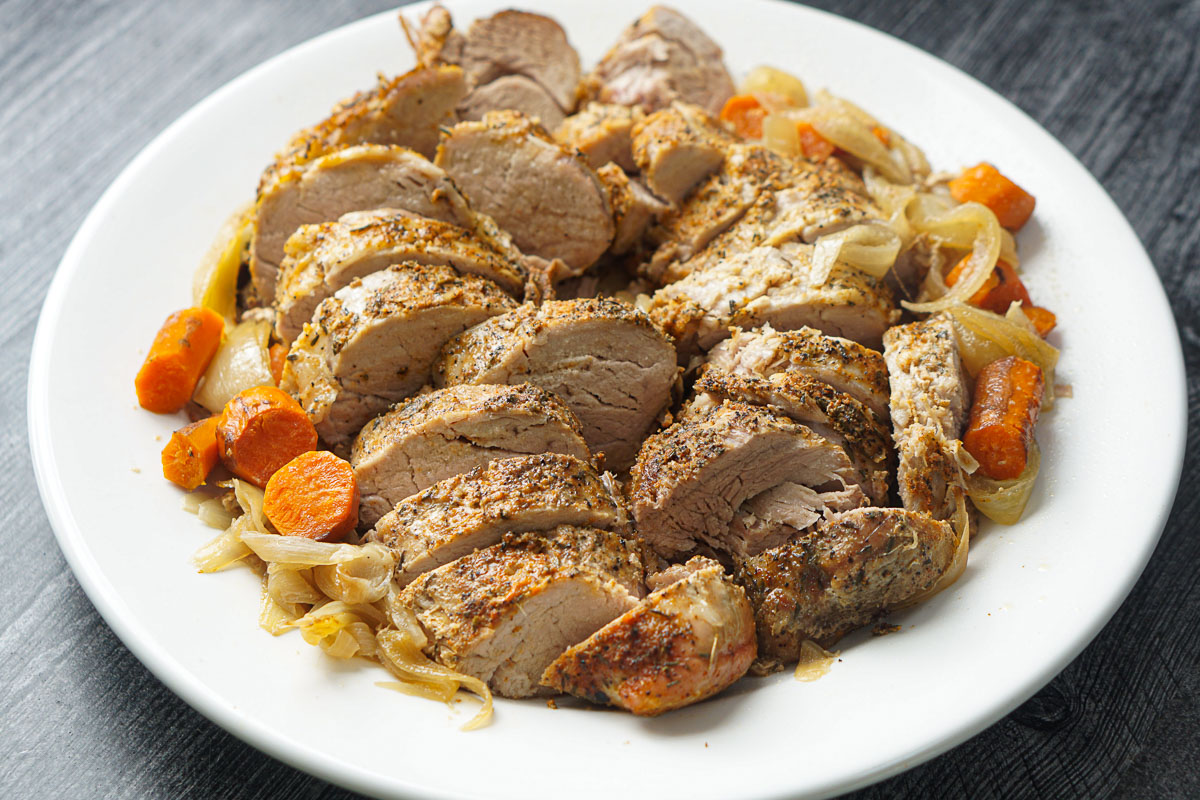 white platter with sliced pork tenderloin and roasted veggies made in slow cooker