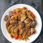 white platter with sliced pork tenderloin and roasted veggies made in slow cooker and text