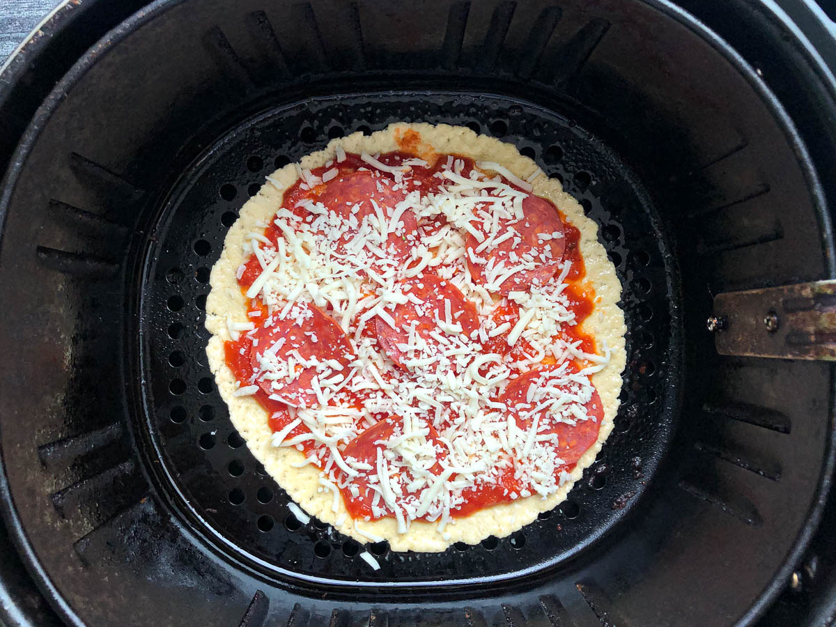 air fryer basket with keto tortilla pizza ready to bake