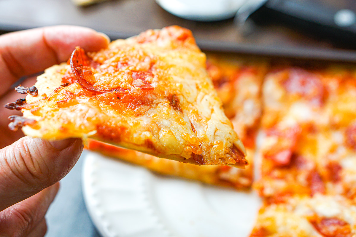 fingers holding a slice of tortilla pepperoni pizza