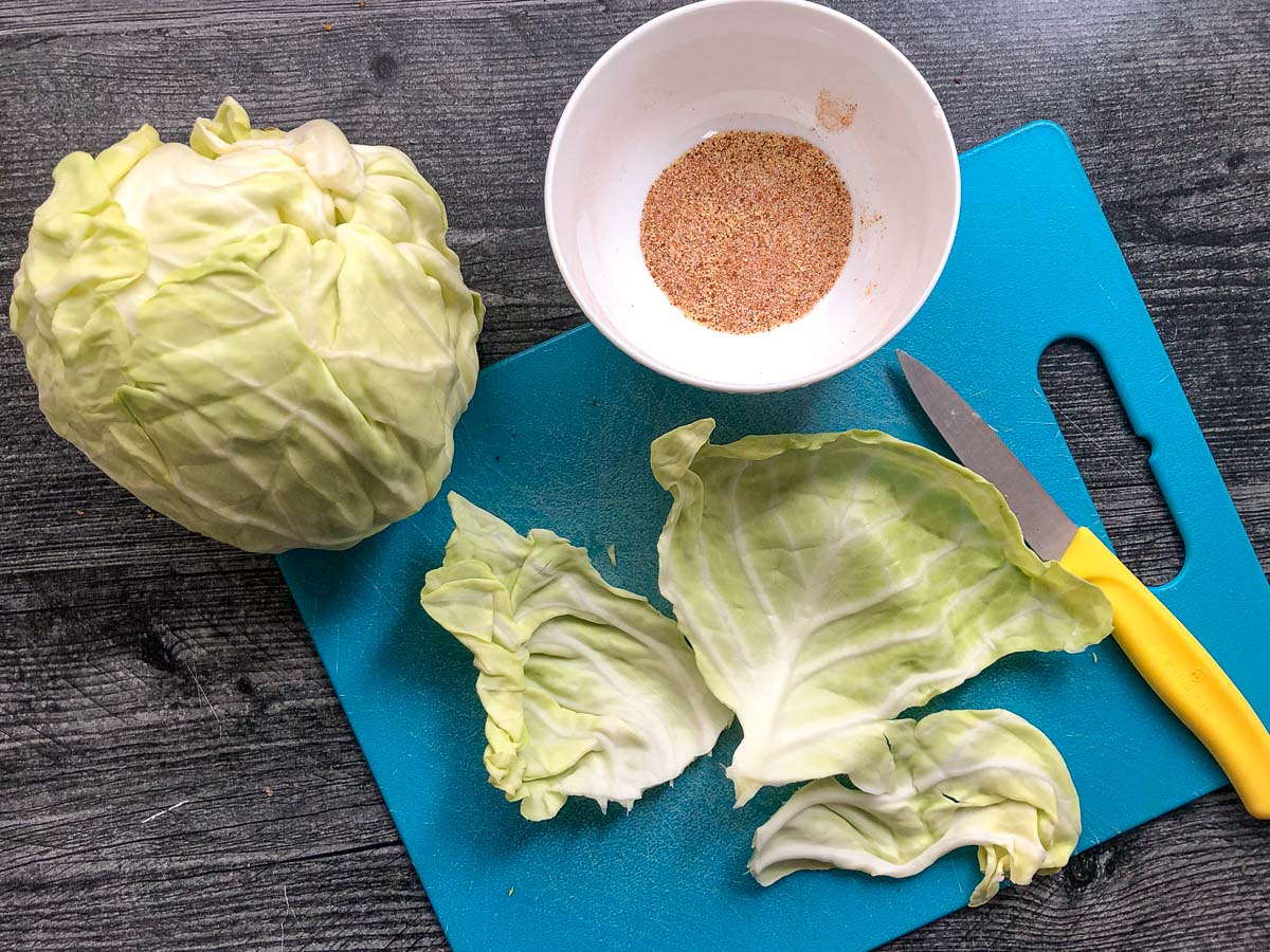 blue cutting board with head of cabbage and leaves and bowl of spices