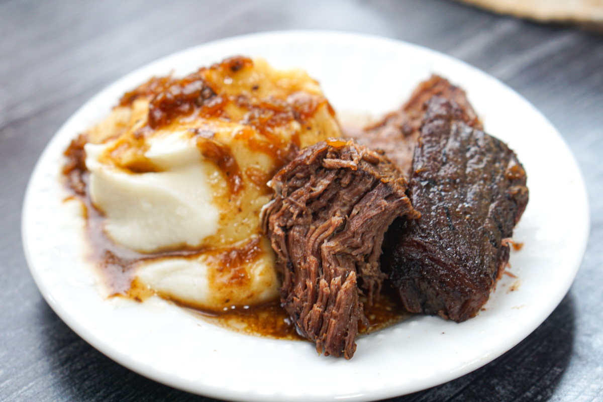 white plate with a piece of the beef roast and mashed cauliflower with gravy