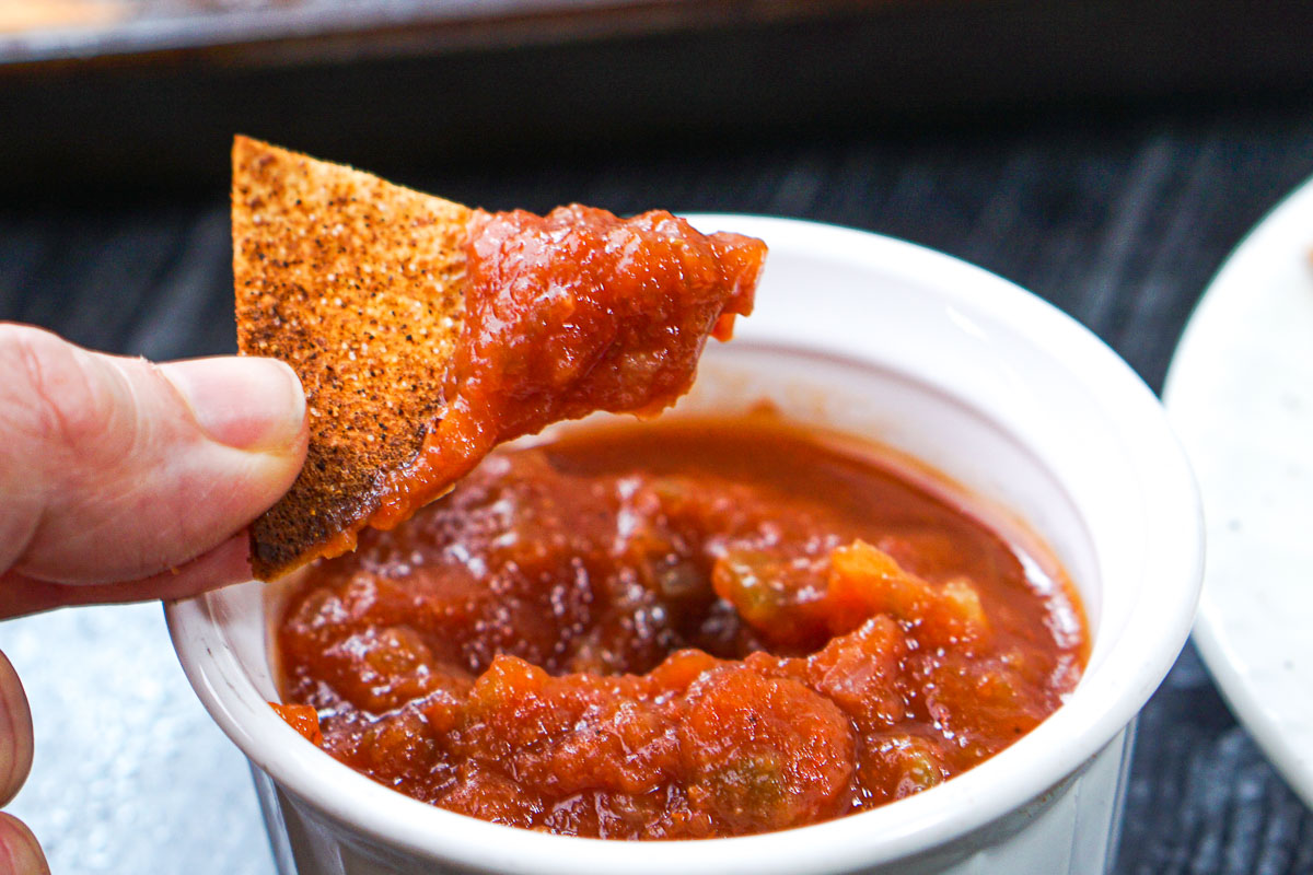 fingers holding a chip dipped in salsa